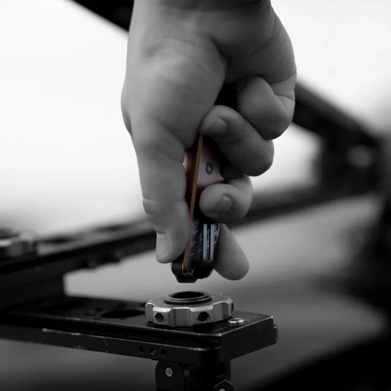 A hand uses a multitool to adjust a metal part on a black mechanical structure.