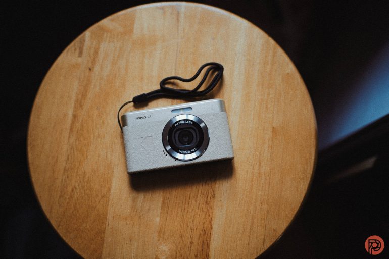 A silver digital camera with a wrist strap sits on a round wooden table.