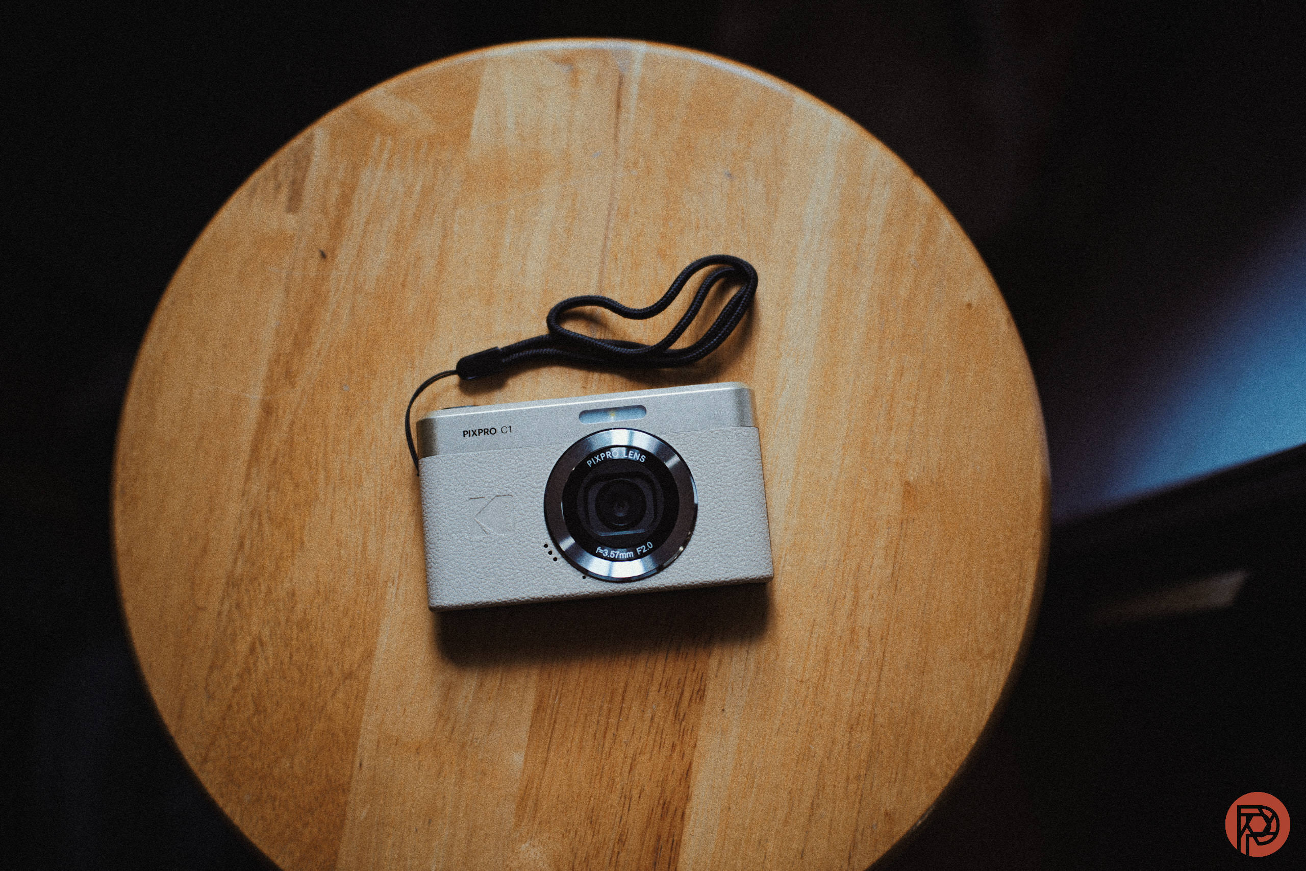 A silver camera with a black strap rests on a round wooden table.