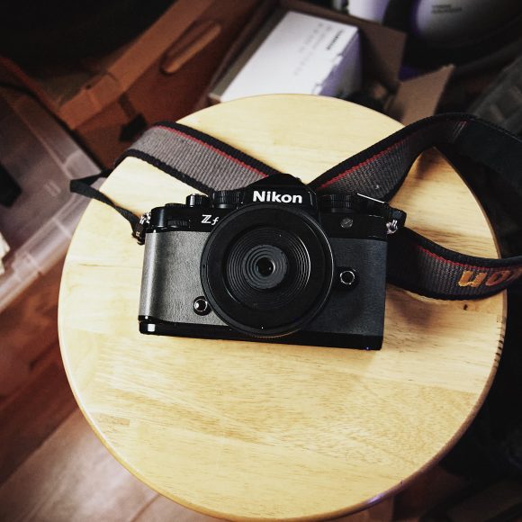 Nikon Z fc camera with a strap resting on a round wooden stool, viewed from above.