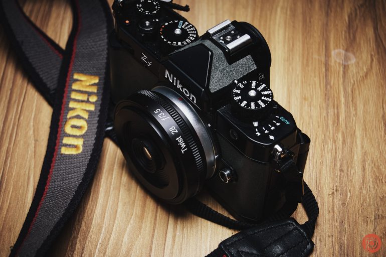 A Nikon Z fc camera with a lens and strap, resting on a wooden surface.