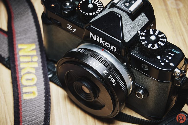 Close-up of a Nikon Z fc camera with a 28mm lens and a Nikon-branded camera strap on a wooden surface.