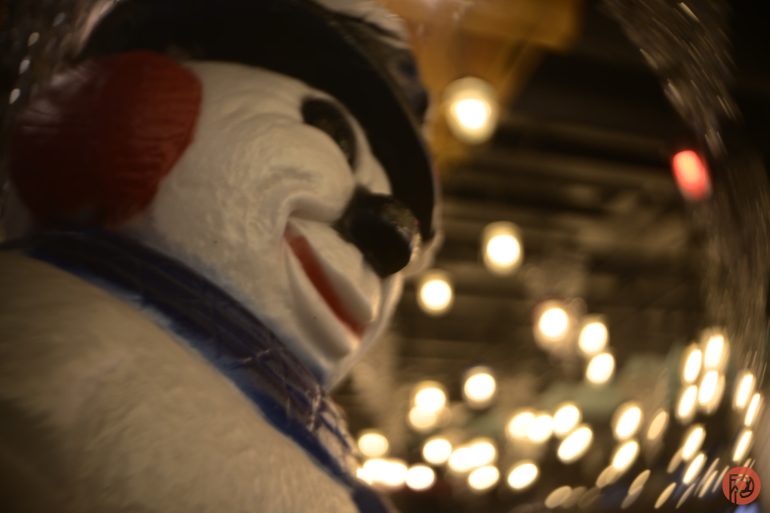 Close-up of a smiling snowman decoration with blurred string lights in the background.