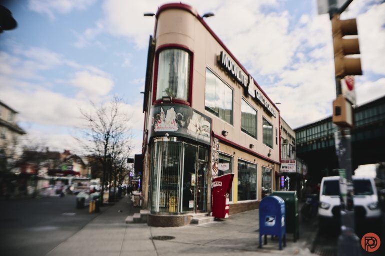 A vintage corner building with a red vending machine and a blue mailbox on a busy city street.