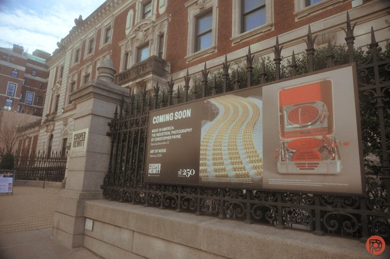 A Coming Soon exhibit sign on a black iron fence outside the Cooper Hewitt museum building.