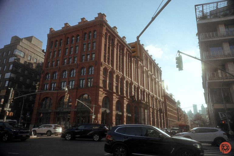 Red-brick historic building on a busy city street corner with cars and traffic lights under a blue sky.