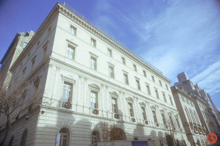 A large, historic white stone building with arched windows under a bright blue, partly cloudy sky.