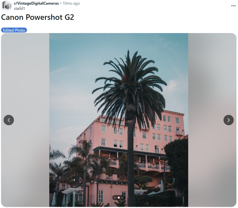 A tall palm tree stands before a pink building under a cloudy sky.