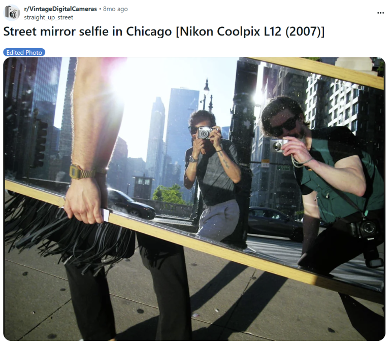 Three people take a selfie in a large mirror on a sunny Chicago street with city buildings in the background.