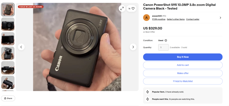 A hand holding a black Canon PowerShot digital camera; eBay listing visible on the right side.