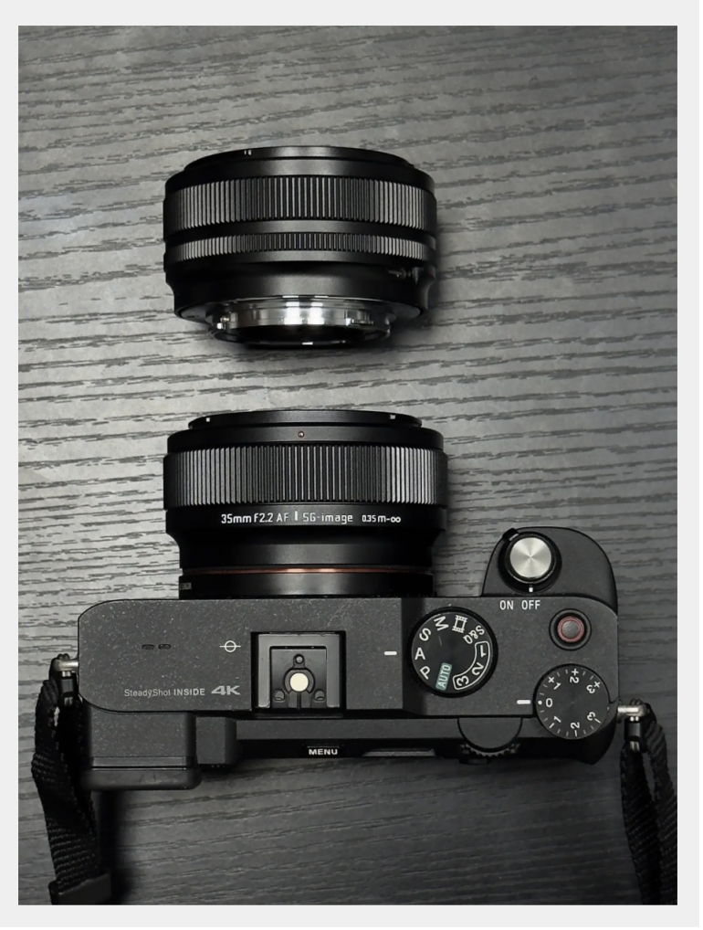 A digital camera with a lens attached and an additional lens placed above it on a dark wooden surface.