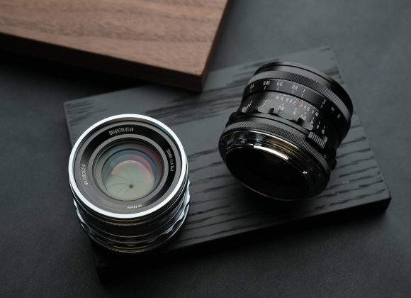 Two camera lenses placed on a dark wooden surface, with a wooden board in the background.