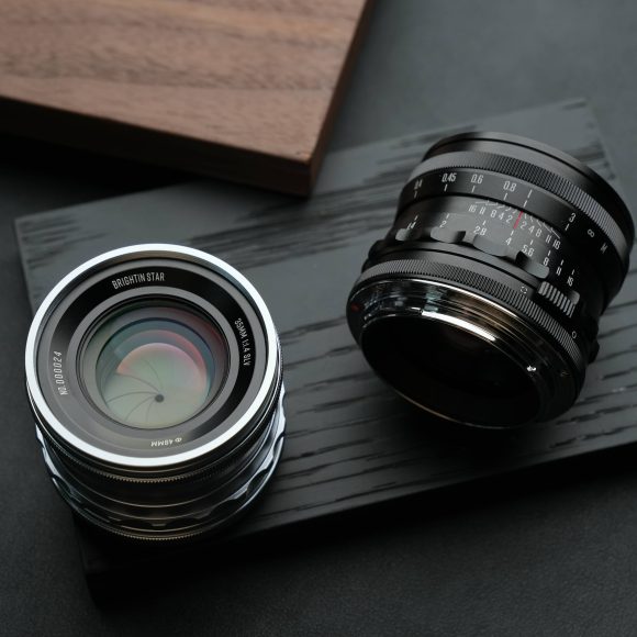 Two camera lenses placed on a dark wooden surface, with a wooden board in the background.