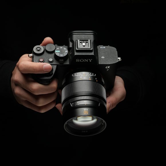 A person holding a Sony Alpha camera with a 50mm lens against a dark background.