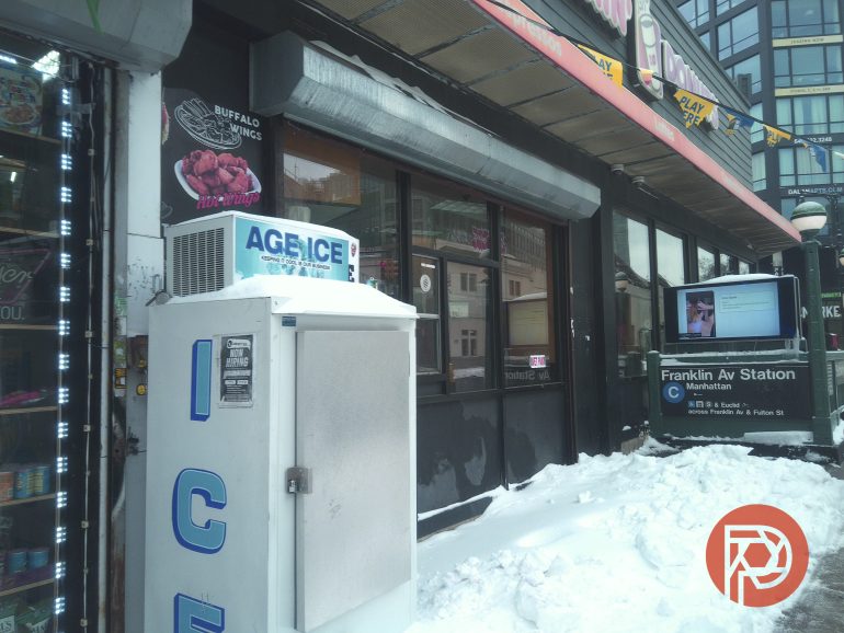 Snowy sidewalk in front of a store with an ice machine, near Franklin Ave subway station entrance in Brooklyn.