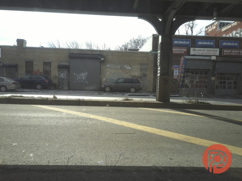 A street view of a closed auto repair shop with graffiti on the metal shutters and parked cars outside.