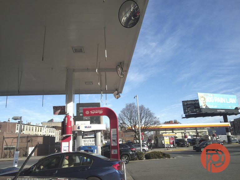 A car at a Mobil gas station pump under a canopy on a clear day, with a billboard in the background.