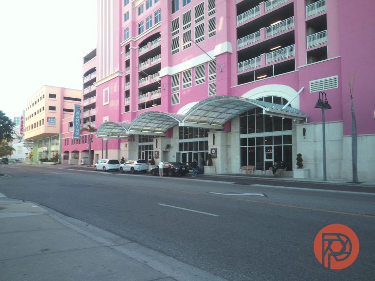 A pink multi-story building with balconies and cars parked along the street in front.