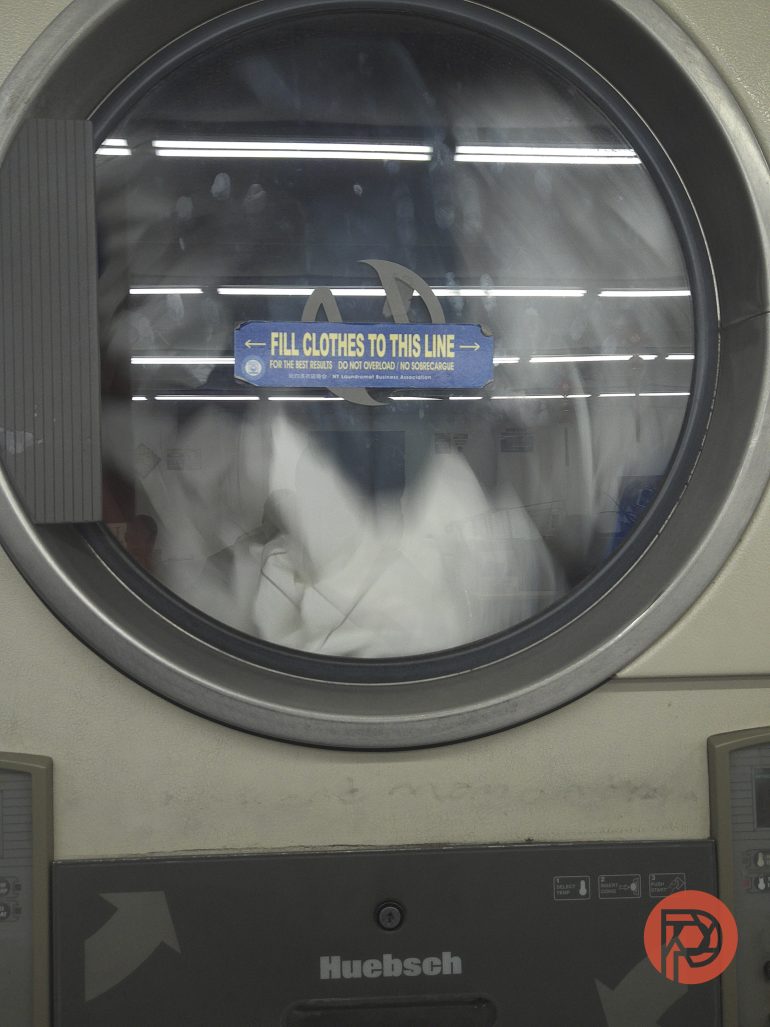 Front view of a washing machine mid-cycle with clothes spinning inside and a fill line sign on the glass door.