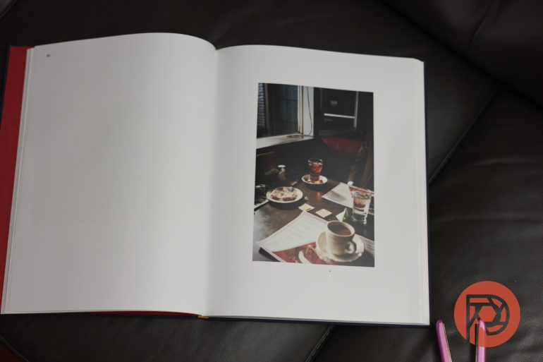 An open book displays a photo of a café table with coffee cups and saucers on a brown leather surface.