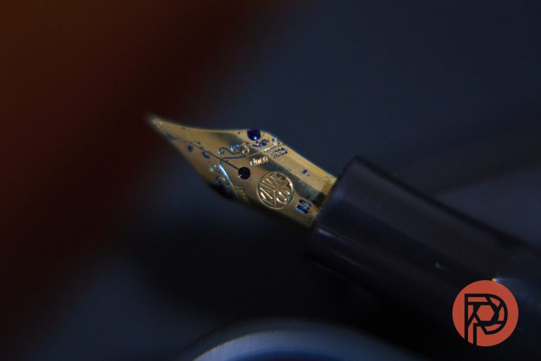 Close-up of a fountain pen nib with blue ink stains, against a dark background.