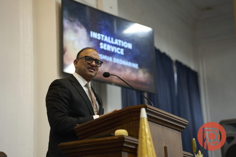 A man in a suit speaks at a podium during an installation service in a church.