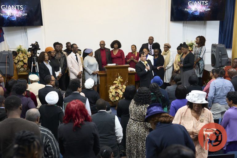 A congregation gathers in a church, with people standing at the front near a podium during a service.