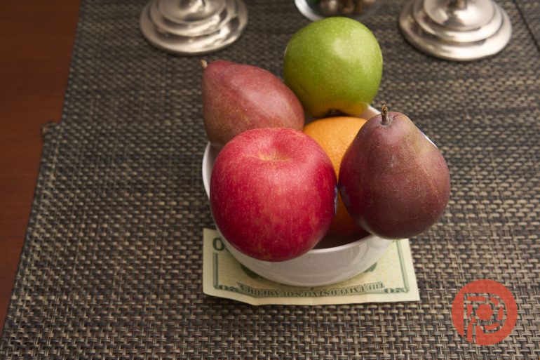 A bowl of assorted fruit sits on a placemat with a $100 bill underneath.