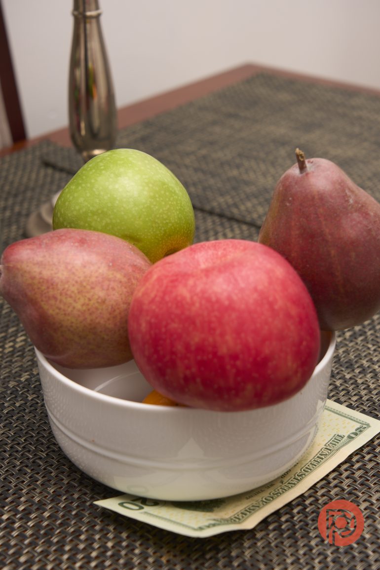 A white bowl with apples and pears on a table, with a dollar bill partially visible underneath.