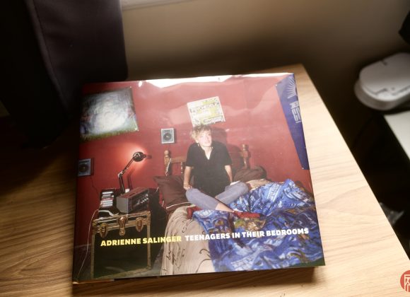 A book titled Adrienne Salinger: Teenagers in Their Bedrooms rests on a wooden surface by a window.