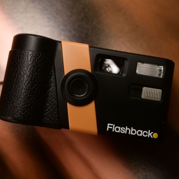 A black and orange Flashback camera rests on a brown and black surface.