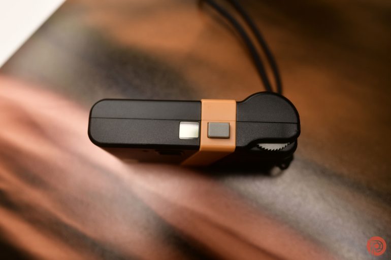 Top view of a compact black and orange camera with a wrist strap, placed on a blurred brown surface.