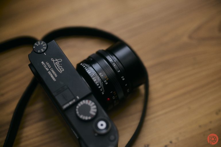 A black Leica camera with a lens and strap rests on a wooden surface.