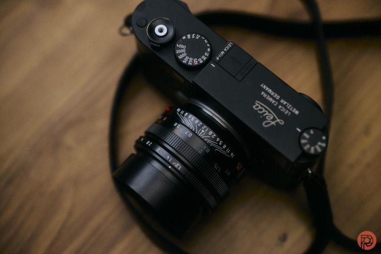 A black Leica camera with a lens and strap rests on a wooden surface.