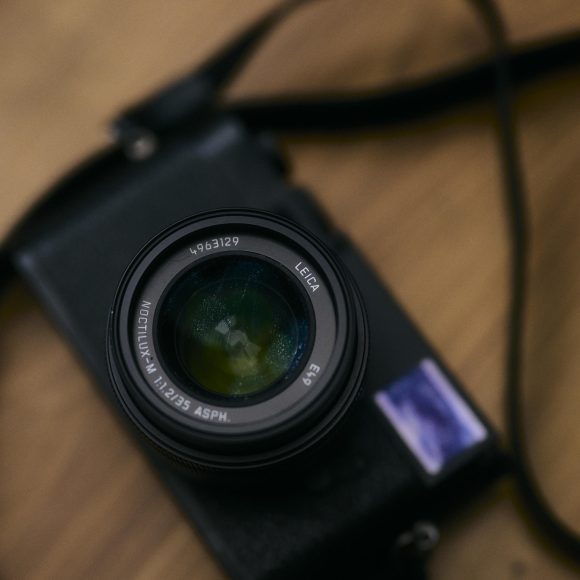 A black Leica camera with a lens and strap rests on a wooden surface.