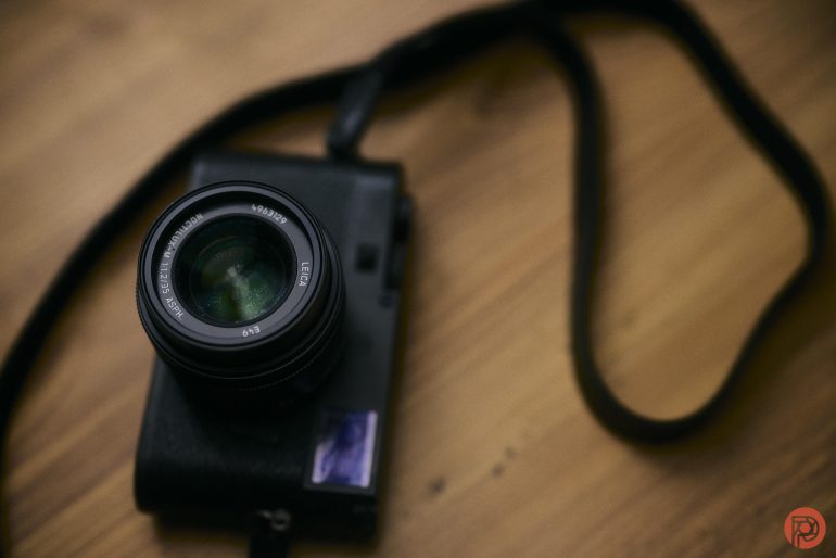 A black camera with a lens and strap rests on a wooden surface.