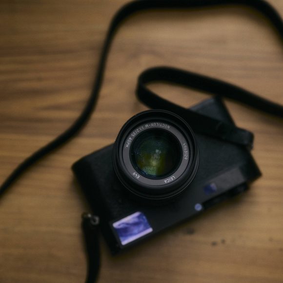 A black camera with a strap rests on a wooden surface, viewed from above.