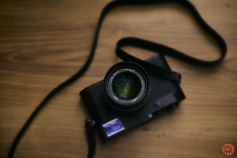 A black camera with a strap rests on a wooden surface, viewed from above.