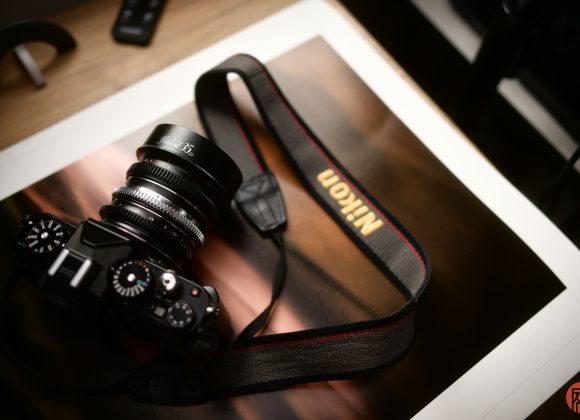 A Nikon camera with a strap rests on top of a glossy photograph on a wooden surface.