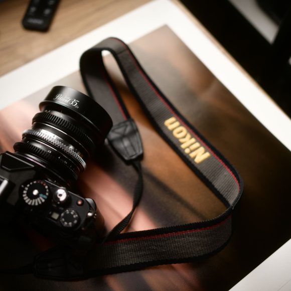 A Nikon camera with a strap rests on top of a glossy photograph on a wooden surface.