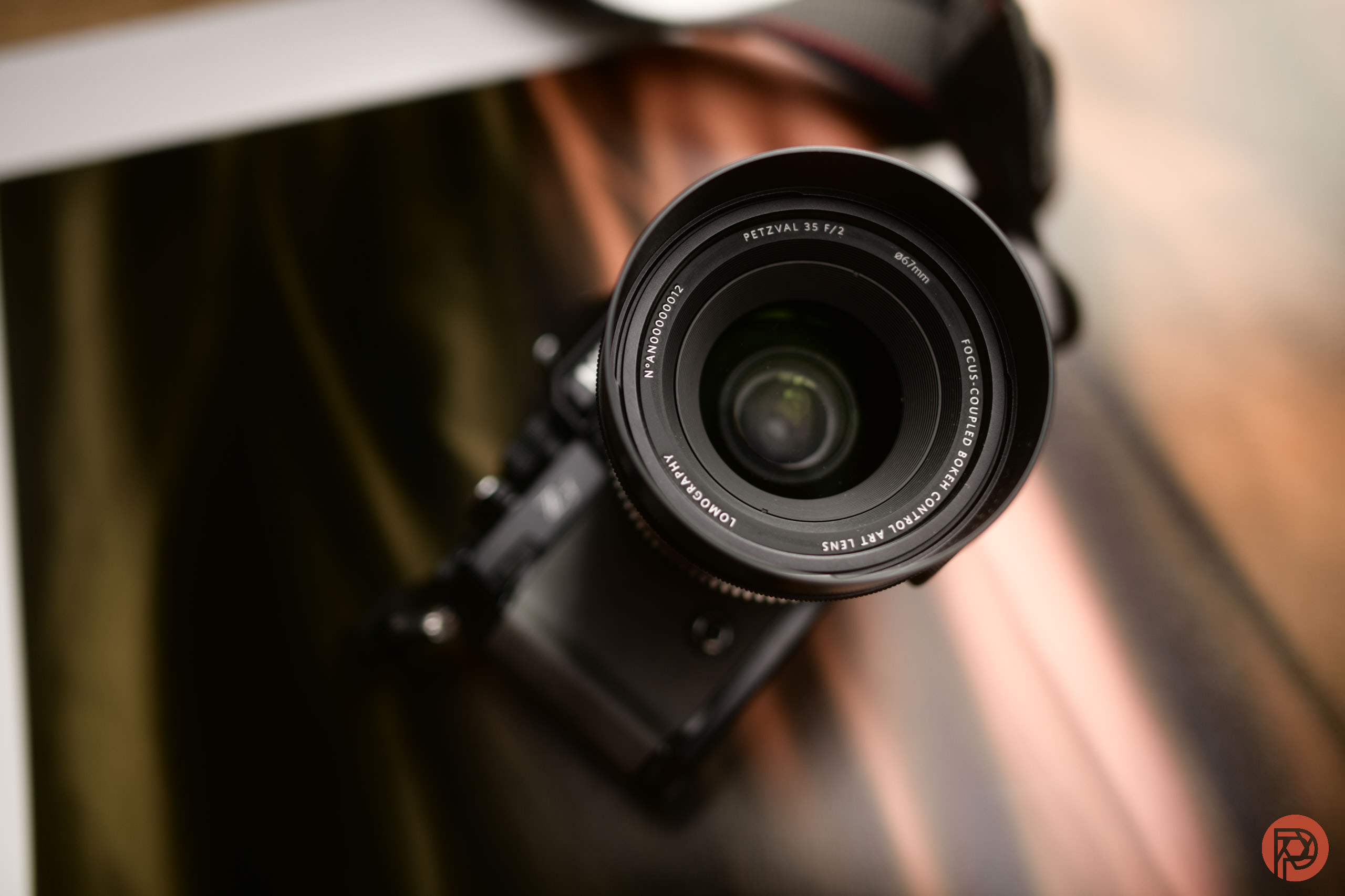 A close-up of a camera lens facing upward, with a blurred background and camera strap visible.