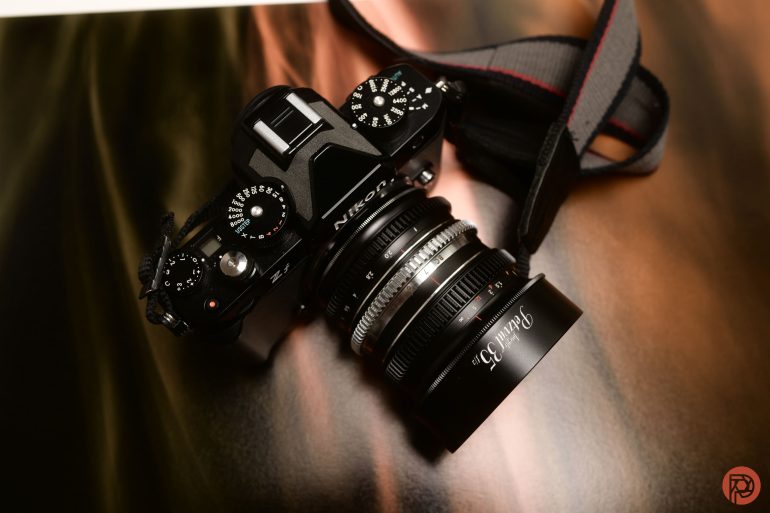 A Nikon camera with a lens and strap resting on a glossy, blurred surface.