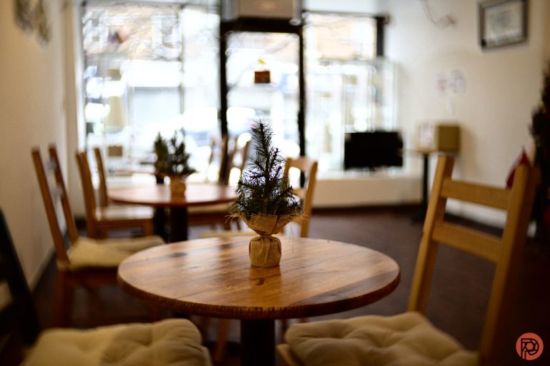 Small potted pine tree centerpiece on a round wooden table in a cozy, softly lit café.