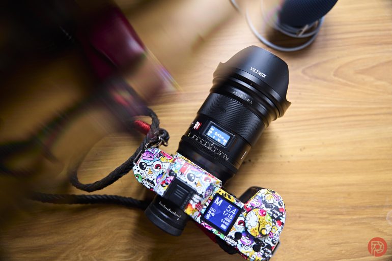 A colorful, sticker-covered camera with a Viltrox lens rests on a wooden surface.