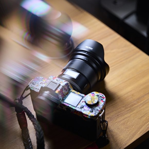 A camera with a colorful, patterned body sits on a wooden table under soft light.