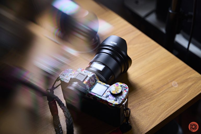 A camera with a colorful, patterned body sits on a wooden table under soft light.