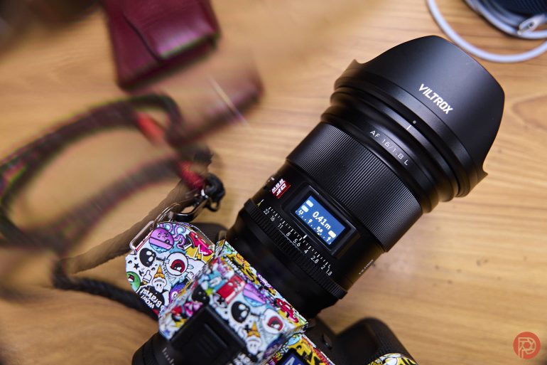 A Viltrox camera lens mounted on a colorful camera, placed on a wooden surface.