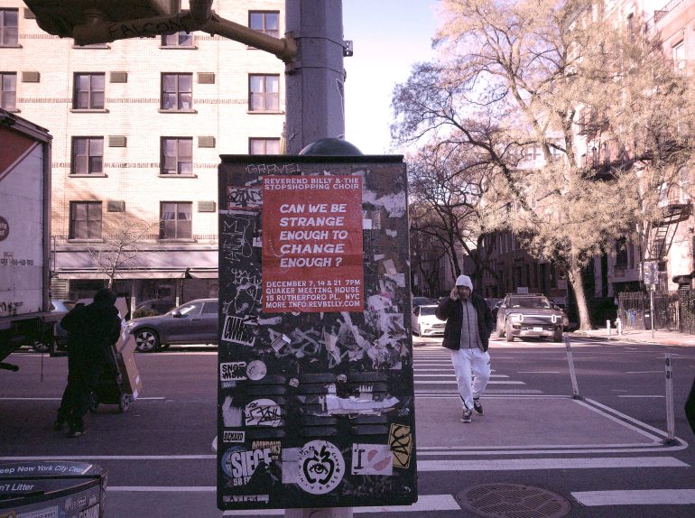 A poster on a sticker-covered utility box on a city street reads, Can we be strange enough to change enough?.