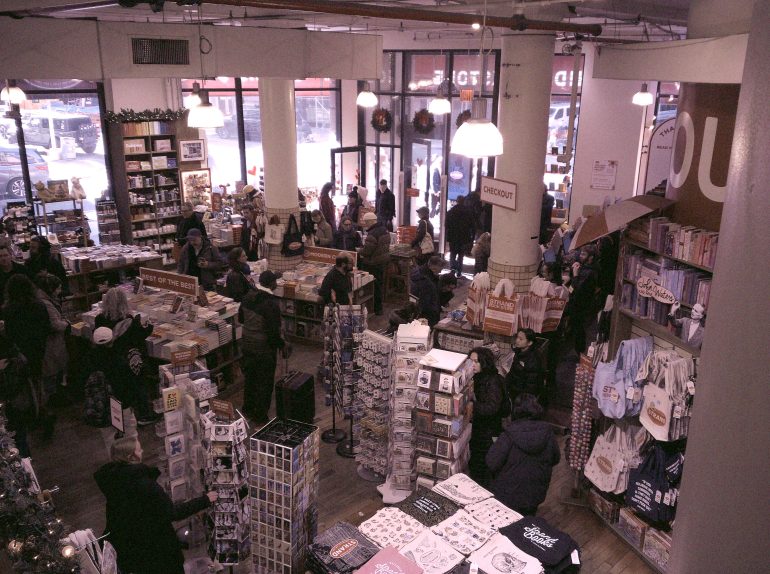 Crowded bookstore with people browsing shelves and displays, near the front entrance and checkout counter.
