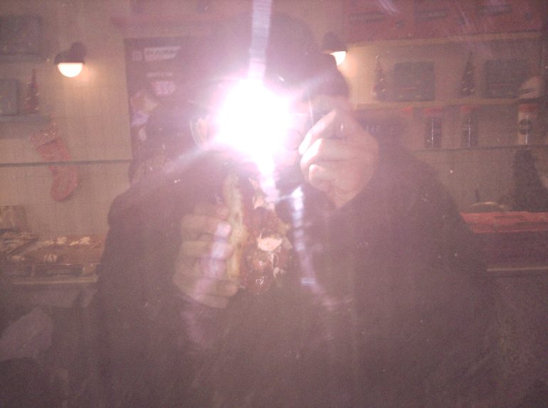 Person holding food faces camera flash, obscuring their face, in a dimly lit restaurant or cafe setting.
